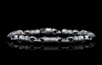 Textured dark silver-toned linked bracelet reflecting on a glossy black surface.