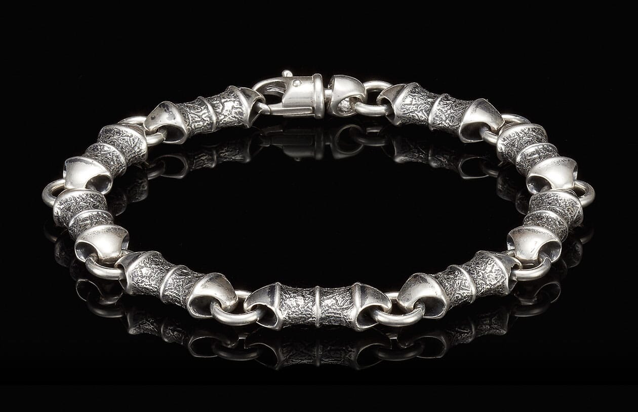 Silver-toned bracelet with alternating textured and smooth cylindrical links, featuring a lobster clasp.