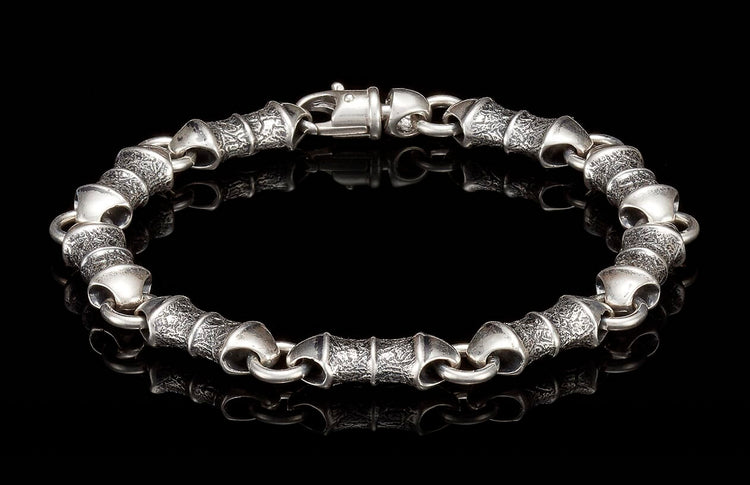 Silver-toned bracelet with alternating textured and smooth cylindrical links, featuring a lobster clasp.