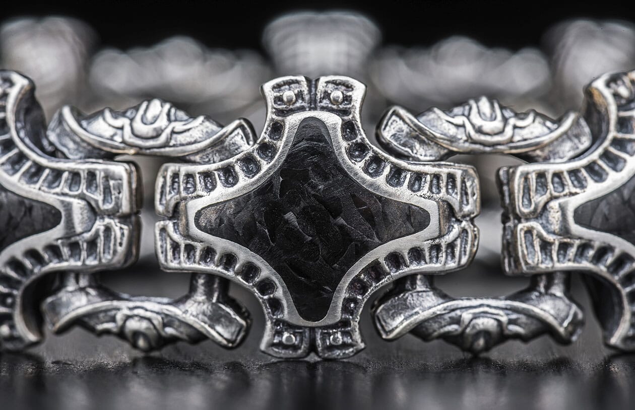 Ornate silver metal jewelry link with a distressed finish and a black textured rhombus-shaped insert, shown in close-up.