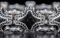 Ornate silver metal jewelry link with a distressed finish and a black textured rhombus-shaped insert, shown in close-up.