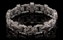 Ornate silver cuff bracelet with intricate carved patterns and a copper-toned accent on the clasp, reflecting on black.