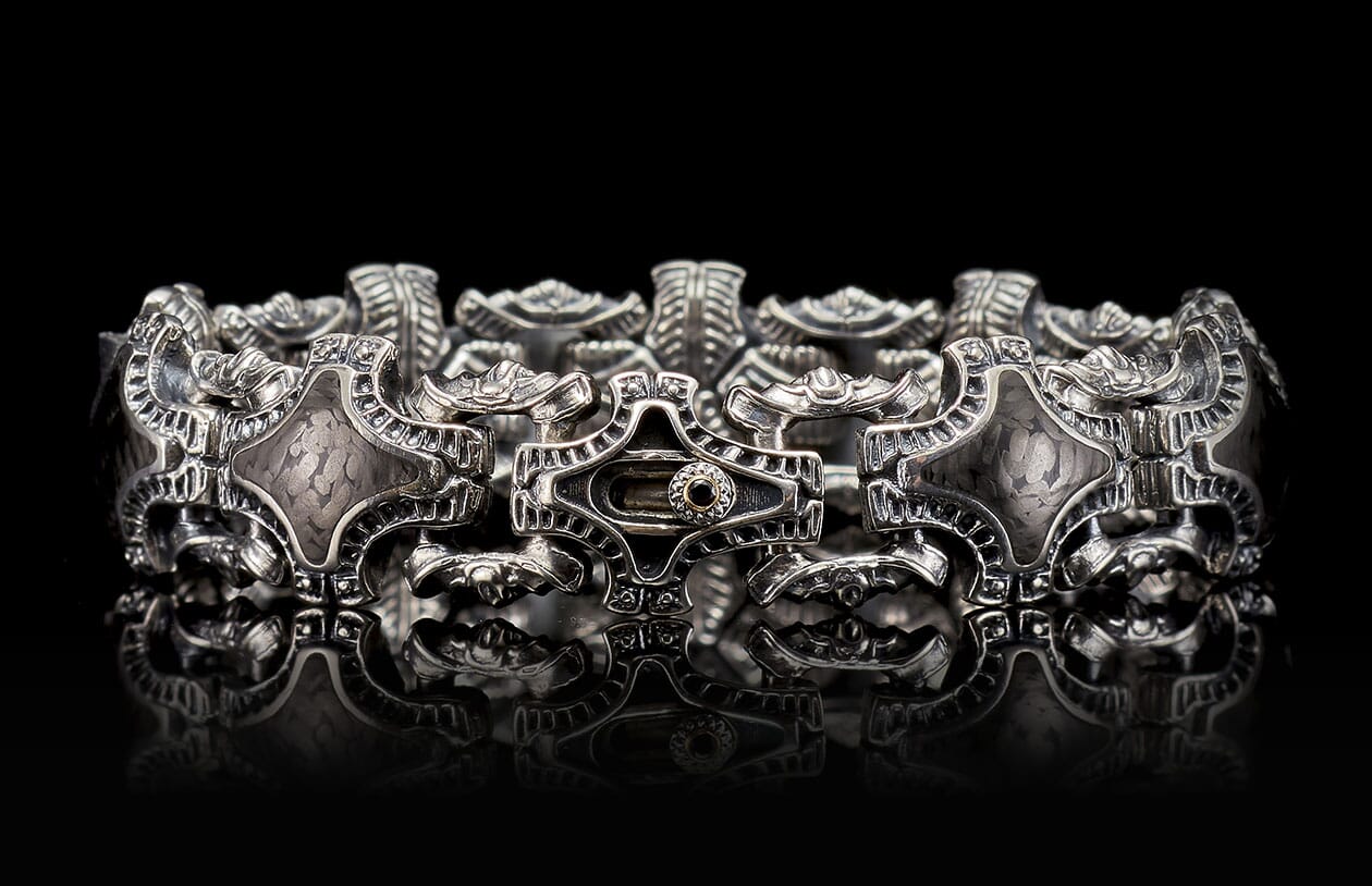 Silver bracelet with ornate, intricate metalwork, textured diamond-shaped links, and a central dark stone detail.