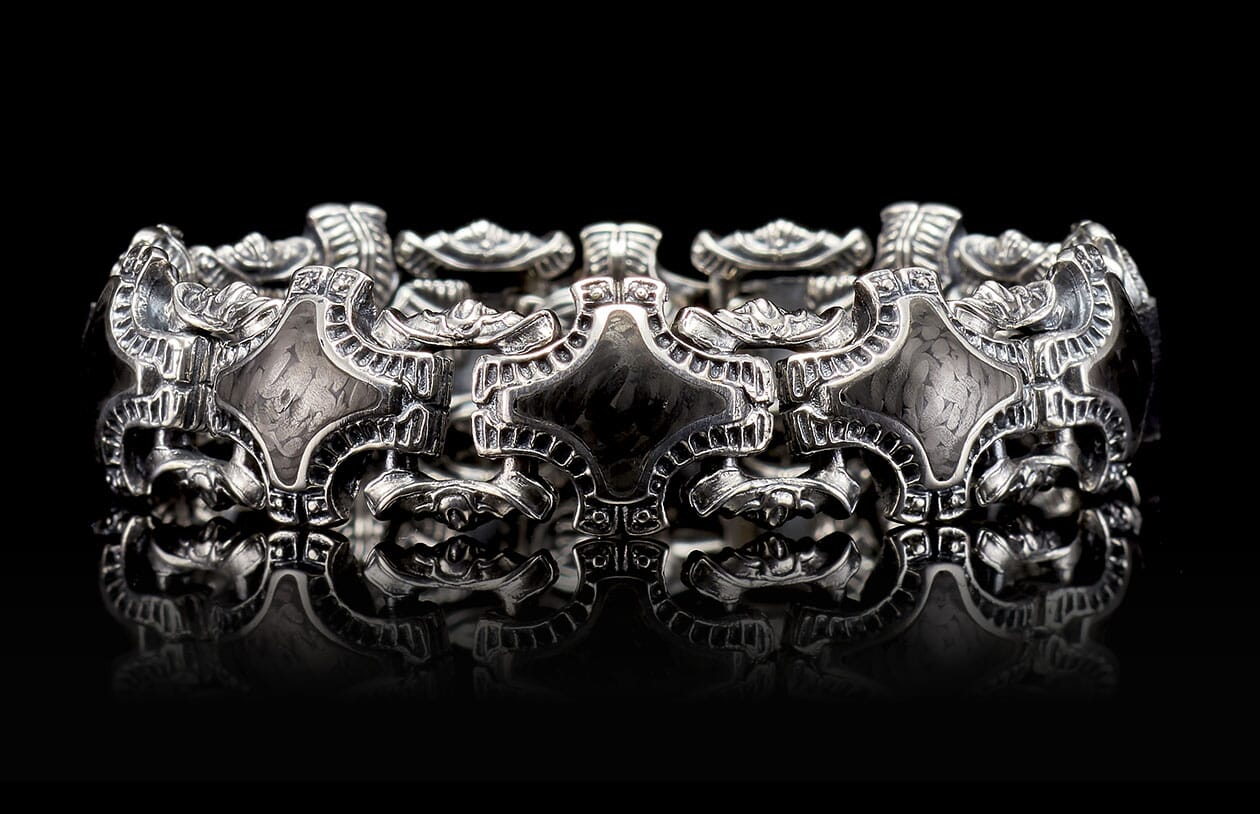 Pawn bracelet in silver-tone metal with ornate scrollwork and shield-shaped links, featuring dark accents and a reflective surface.