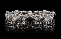 Pawn bracelet in silver-tone metal with ornate scrollwork and shield-shaped links, featuring dark accents and a reflective surface.