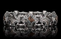 Ornate silver bracelet with geometric links, inlaid with patterned gray and brown stones, reflected on a black surface.