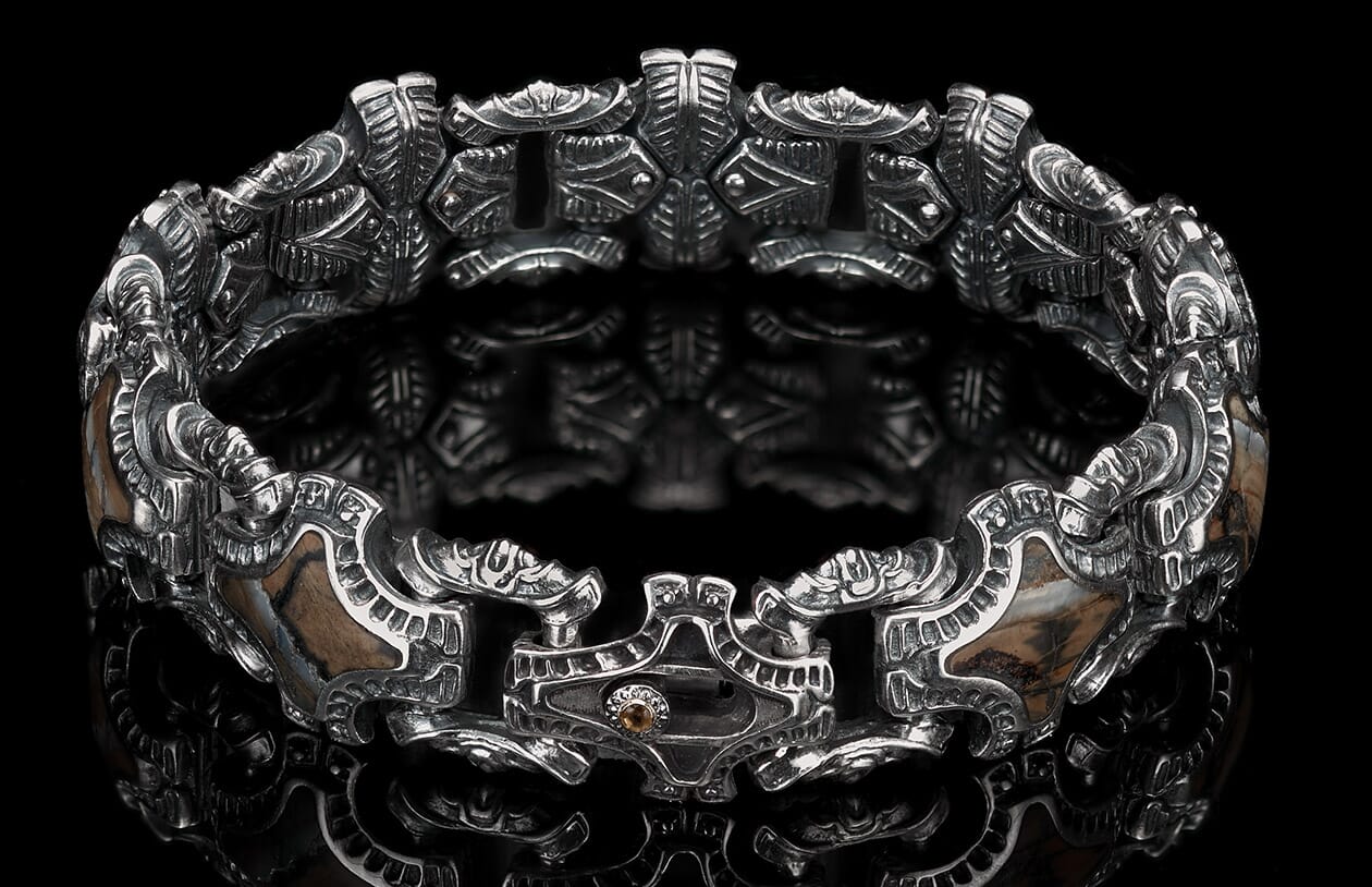 Ornate silver bracelet with intricate metalwork and textured brown stone inserts, featuring a central clasp with a small amber gem.