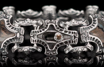 Ornate silver bracelet with intricate links, dark brown inlays, and a central brown gemstone.