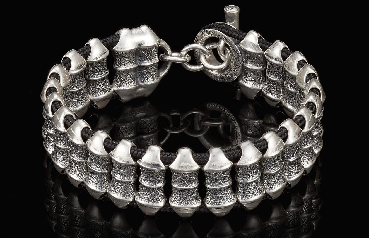 Silver bracelet with textured, ribbed beads on a black cord, featuring a toggle clasp.