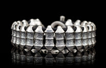 Chunky silver bracelet with textured barrel links and a black cord, reflecting on a dark surface.