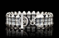 Silver-toned metal bracelet with black braided cord, barrel beads featuring a cracked texture, and a toggle clasp.