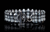 Dark silver bracelet with rugged textured metal segments and black cord, featuring a toggle clasp.