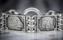 Silver-toned bracelet with embossed bear heads in profile and frontal views, connected by interwoven chain links.