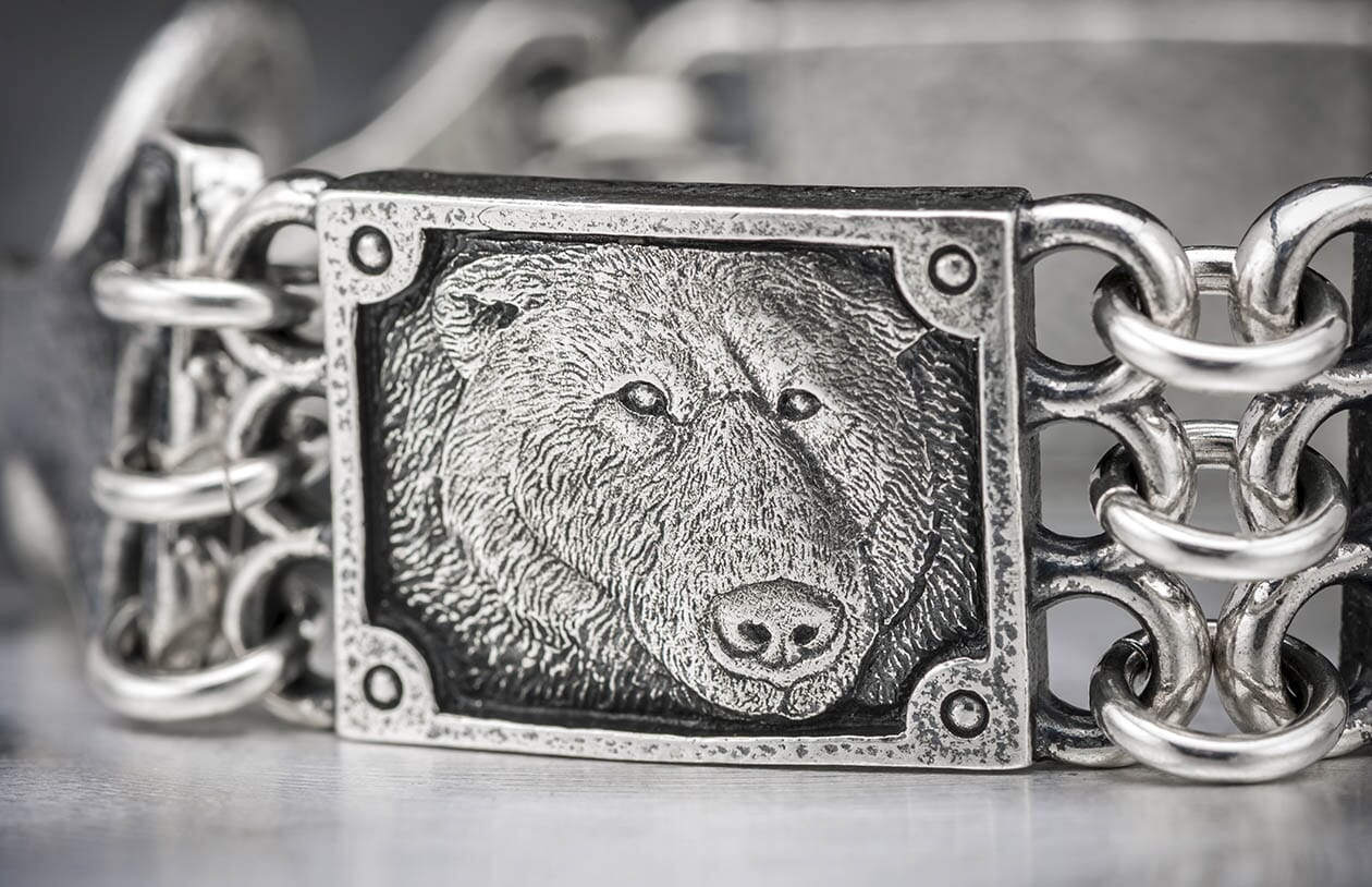 Close-up of a silver bracelet featuring a textured bear head panel and interlocking chain links.