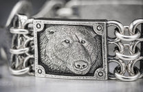 Close-up of a silver bracelet featuring a textured bear head panel and interlocking chain links.