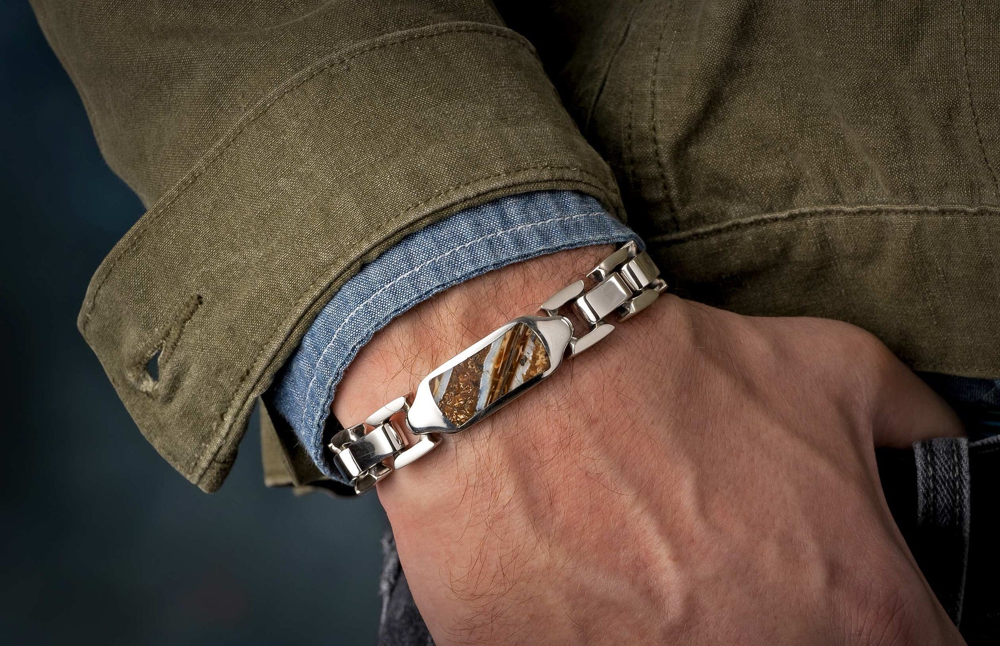 Silver-toned link bracelet with a rectangular mammoth ivory inlay on a man's arm wearing a blue denim shirt and green jacket.