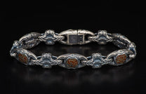 Silver bracelet with reddish-brown, cracked inlays, featuring intricate scrollwork and ornate, stylized skull links, laid flat.