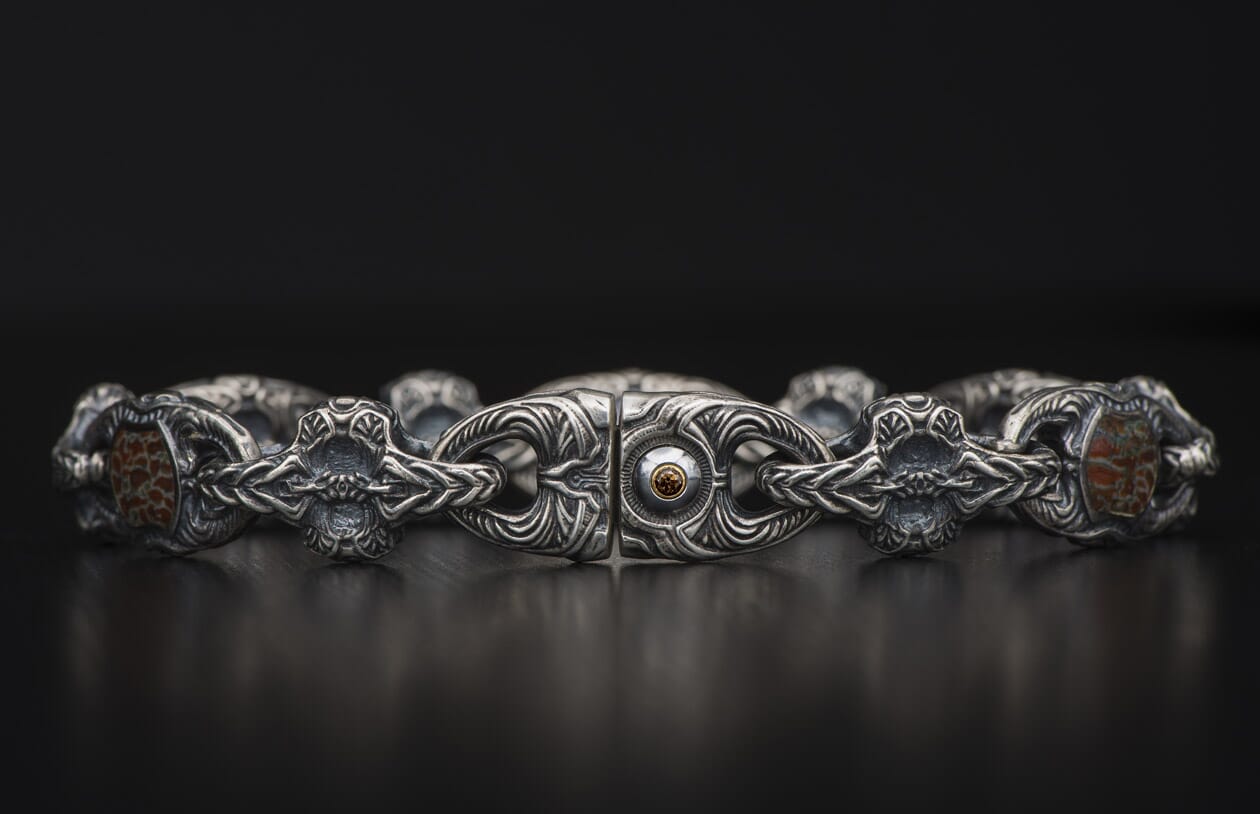 A silver bracelet with intricately carved links, featuring reddish-brown patterned stones and a central amber-colored gem.