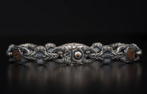 A silver bracelet with intricately carved links, featuring reddish-brown patterned stones and a central amber-colored gem.