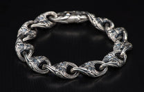 Silver ornate link bracelet featuring intricate carvings on each thick, interconnected link, against a dark background.
