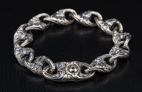 Ornate silver chain bracelet with intricate swirling patterns on each link and a dark gem in the central clasp.