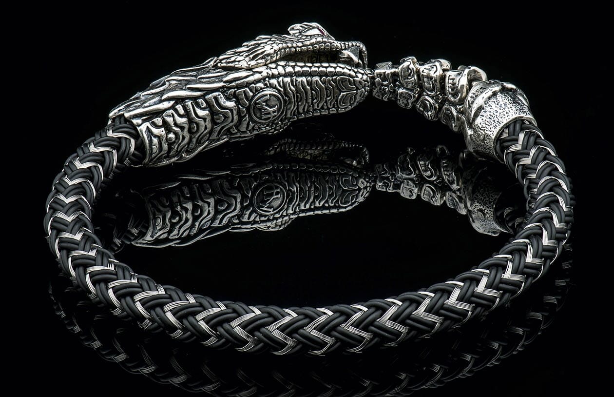 Black and silver braided Lancehead bracelet with an ornate silver snake head clasp and intricate texture, on a reflective surface.