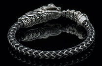 Black and silver braided Lancehead bracelet with an ornate silver snake head clasp and intricate texture, on a reflective surface.