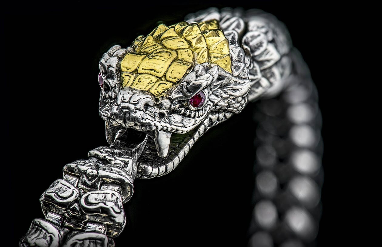 Silver snake-head bracelet with gold-toned scales and red ruby eyes, mouth slightly open showing fangs.