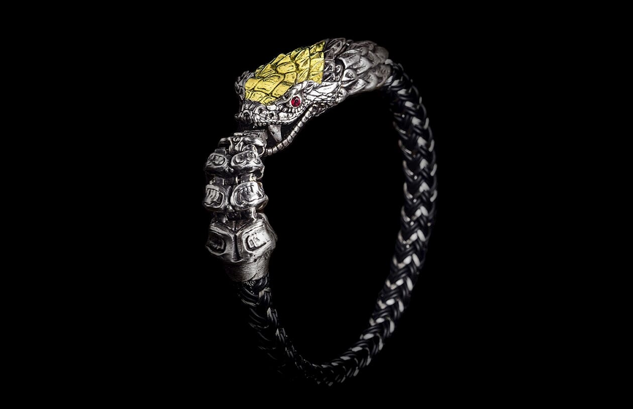 Silver snake head bracelet with yellow scales, red eyes, and a braided black and white band.