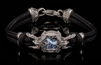 Black braided cord and silver bracelet with an ornate central medallion, white and black patterned stone, flanked by dragon heads, and intricate clasp.