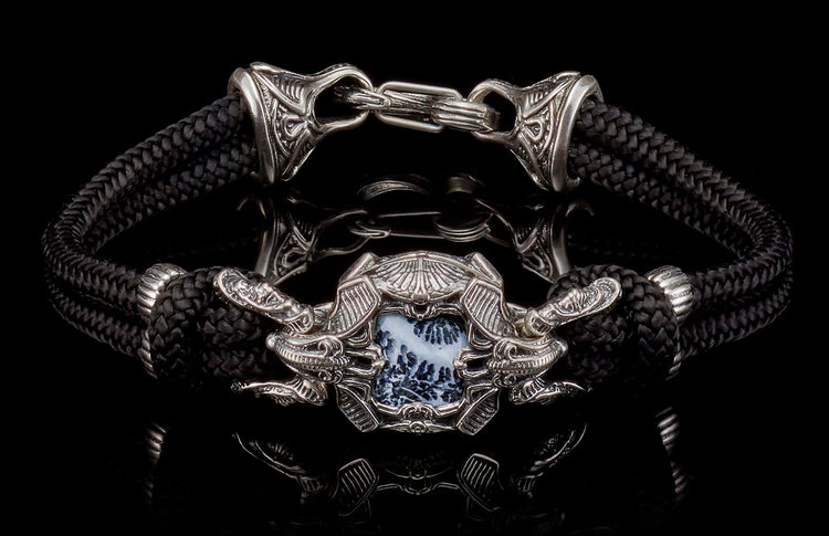 Black braided cord and silver bracelet with an ornate central medallion, white and black patterned stone, flanked by dragon heads, and intricate clasp.