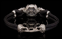 Black braided cord bracelet featuring an ornate silver-toned stylized helmet centerpiece and decorative hook clasp.