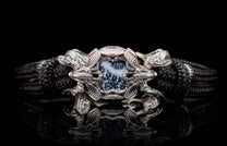 Ornate silver-toned bracelet with a black braided band and a central black and white dendritic stone framed by stylized dragon heads.