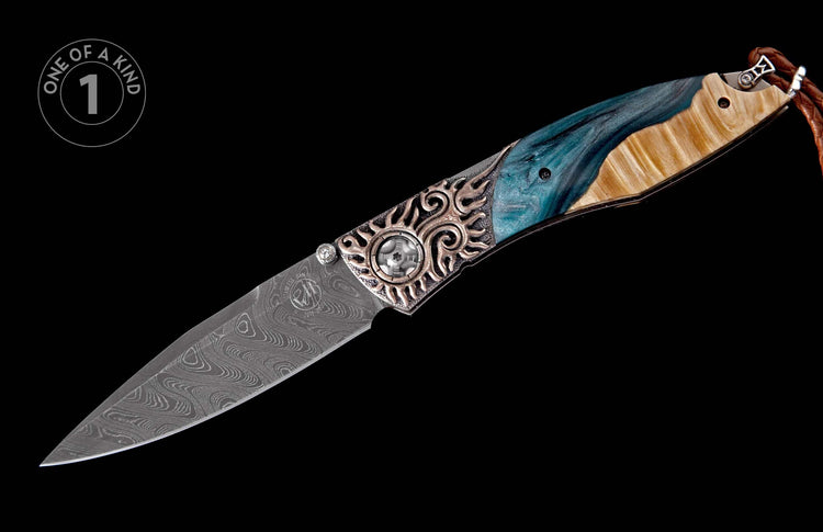 Damascus steel folding knife with an ornate silver-toned bolster, blue resin, and light wood handle, featuring a braided leather lanyard.