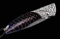 Ornate folding knife with a carved silver eagle head bolster, dark blue and brown handle, Damascus blade, and braided black leather lanyard.