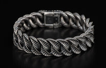 Silver bracelet with intricate leaf-like textured links laid on a dark surface.