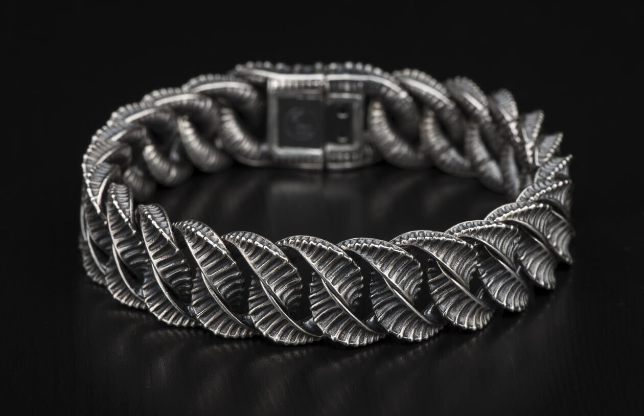 Silver bracelet with intricate leaf-like textured links laid on a dark surface.