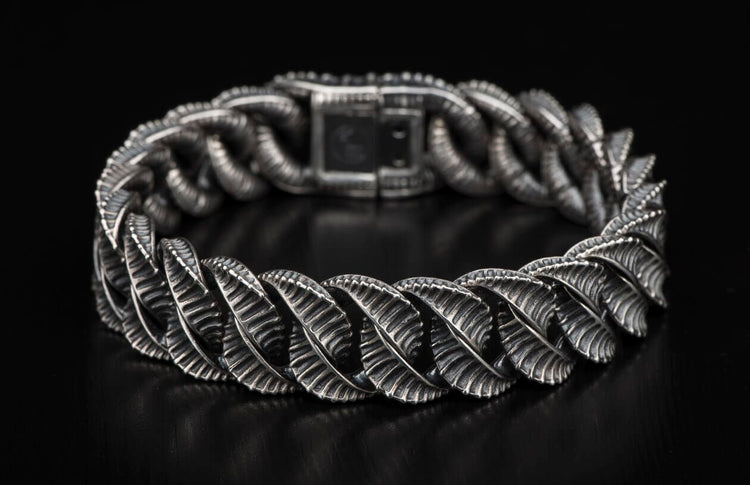 Silver bracelet with intricately textured, ridged links forming a woven pattern, displayed on a dark surface.