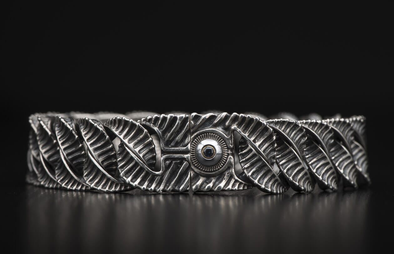 Oxidized silver bracelet with intricate leaf-like links and a central ribbed clasp featuring a dark gem.
