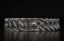 Oxidized silver bracelet with intricate leaf-like links and a central ribbed clasp featuring a dark gem.