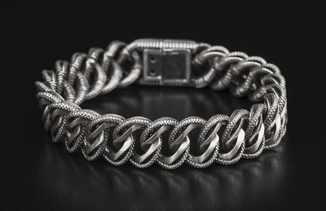 Silver chain bracelet with intricately textured links and a rectangular push-button clasp, displayed curving.