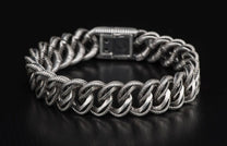 Silver chain bracelet with intricately textured links and a rectangular push-button clasp, displayed curving.