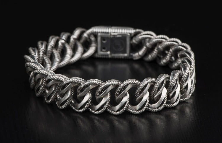 Silver chain bracelet with intricately textured links and a rectangular push-button clasp, displayed curving.