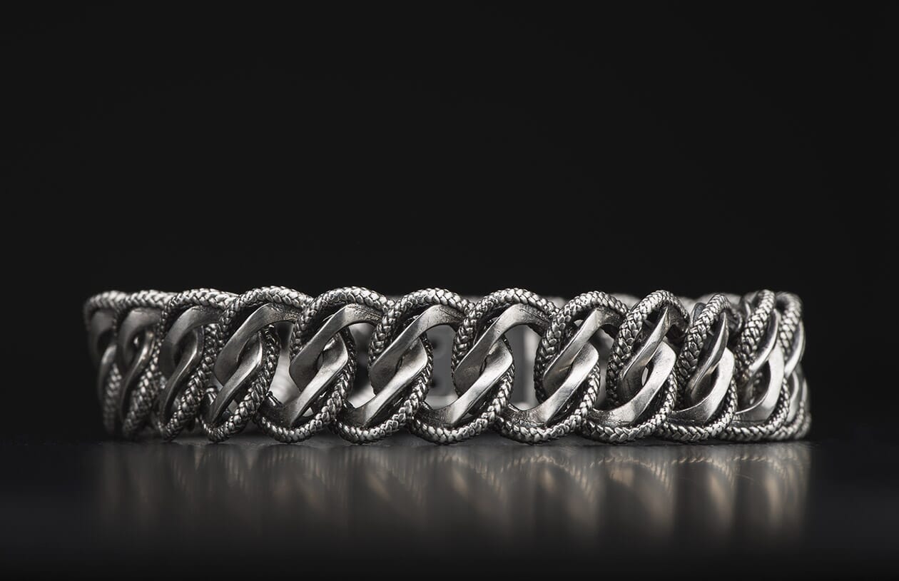 Silver-toned Pasha bracelet with interlocking smooth and braided chain links, reflecting on a dark surface.