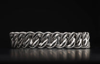 Silver-toned Pasha bracelet with interlocking smooth and braided chain links, reflecting on a dark surface.