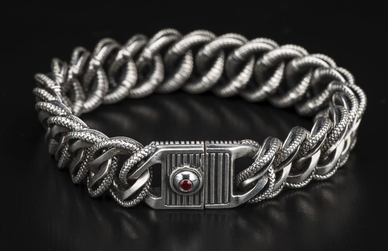 Silver-tone chunky chain bracelet with braided textured links and a decorative clasp featuring a red gemstone.