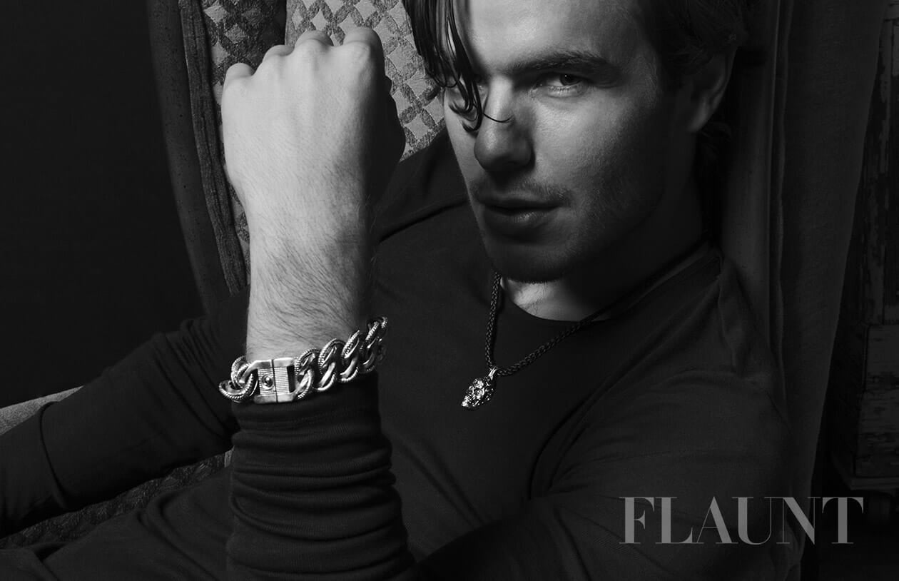 Thick silver-toned chain bracelet and skull pendant necklace worn by a man in a black and white lifestyle shot.