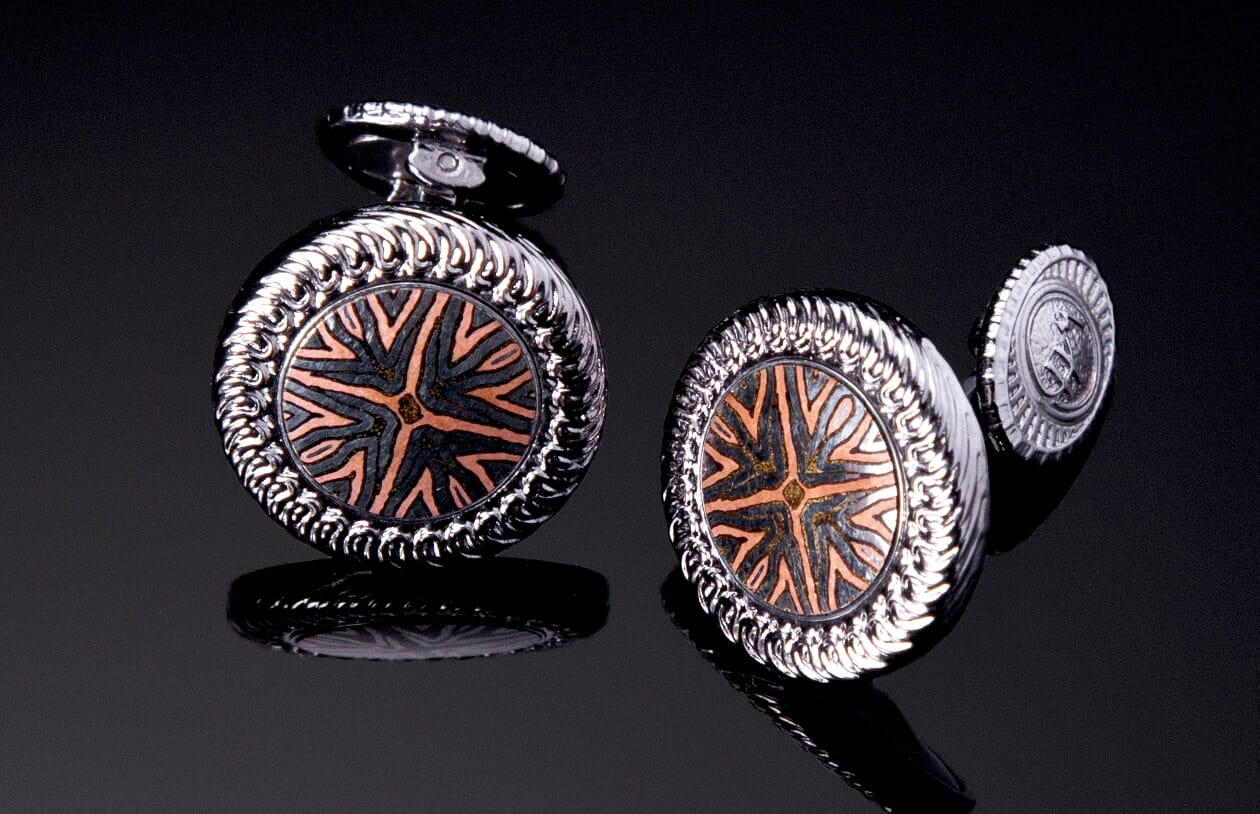 Silver-toned cufflinks with a radial mokume pattern in black and copper, featuring textured rope-like edges.
