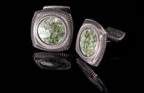 Two square silver cufflinks with mottled green stone inlays and wavy embossed borders, reflected on black.
