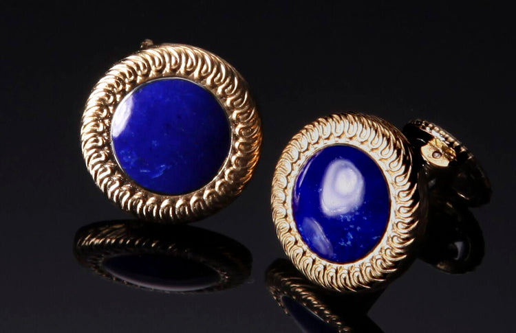 Lapis lazuli cufflinks with ornate gold bezels, reflecting on a dark surface.